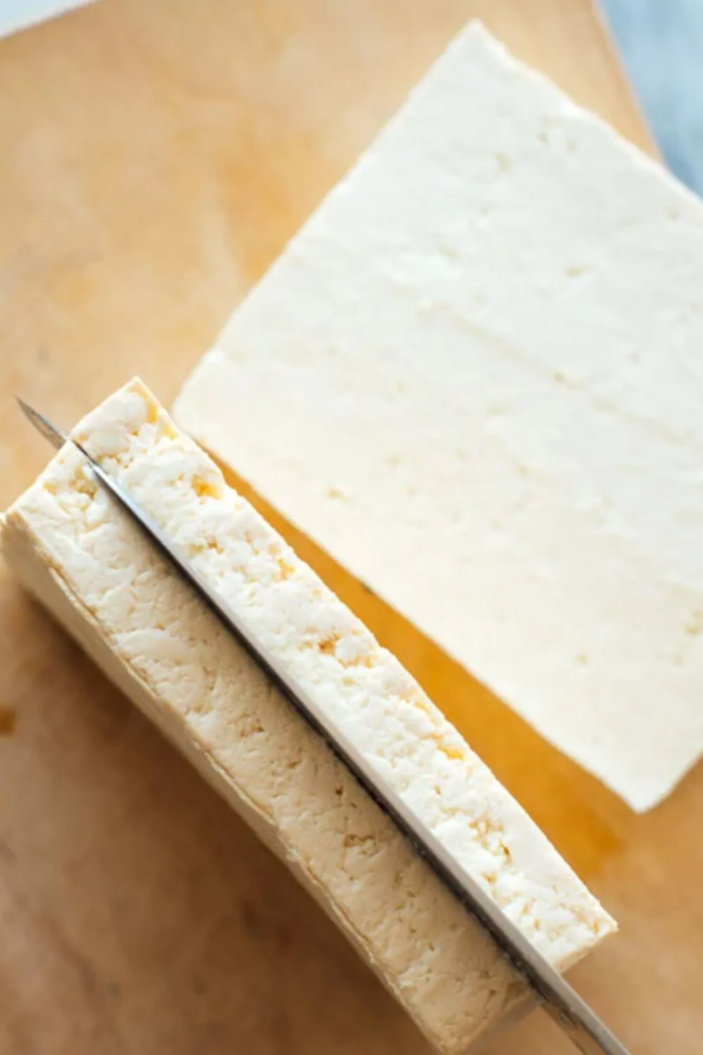Firm tofu block being sliced lengthwise on cutting board