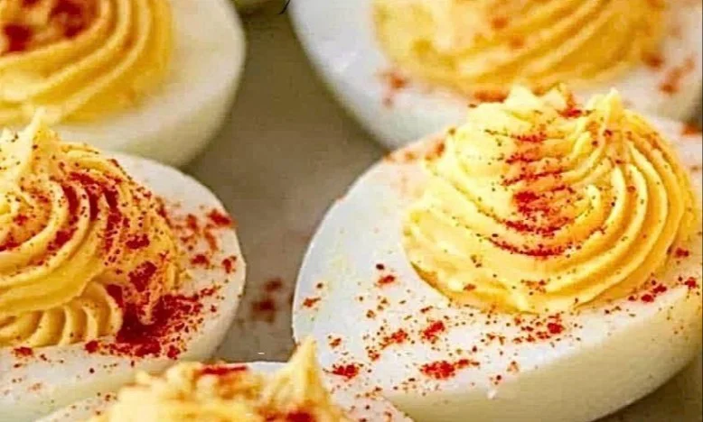 Platter of creamy deviled eggs garnished with paprika and herbs.