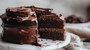 whole gluten free chocolate cake with one slice cut out on white stand