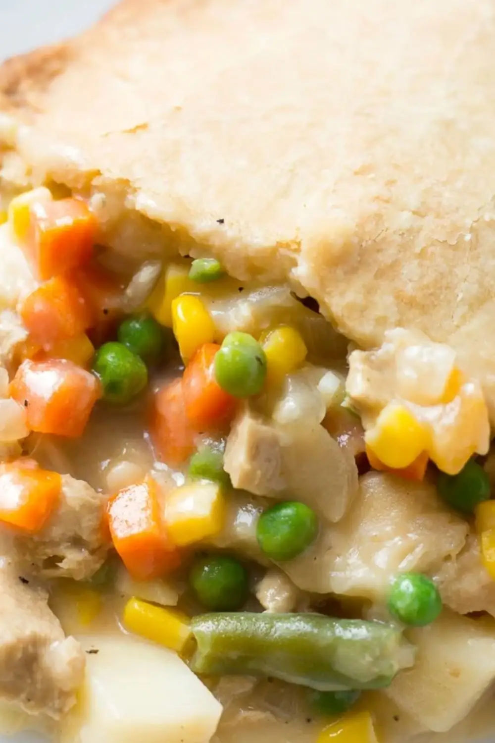 closeup of a vegan pot pie slice showing peas, carrots, and corn under golden crust